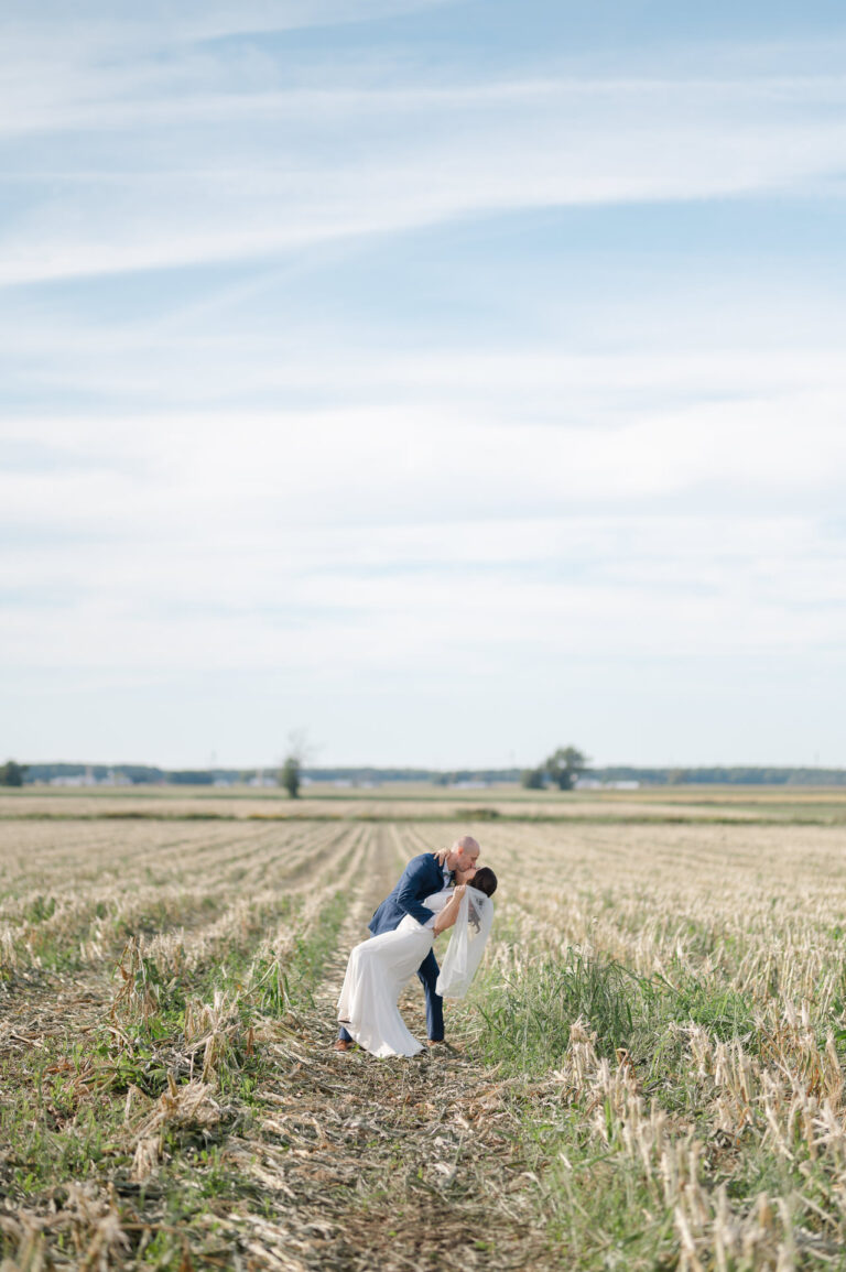 The bride and groom kiss in the middle of a cornfield in a country wedding