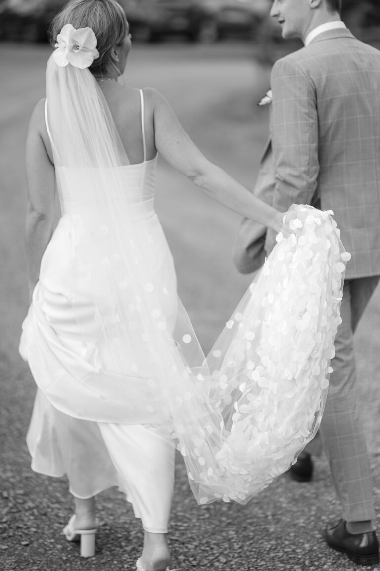 Photo taken au naturel as the bride and groom walk and the bride holds her long veil.